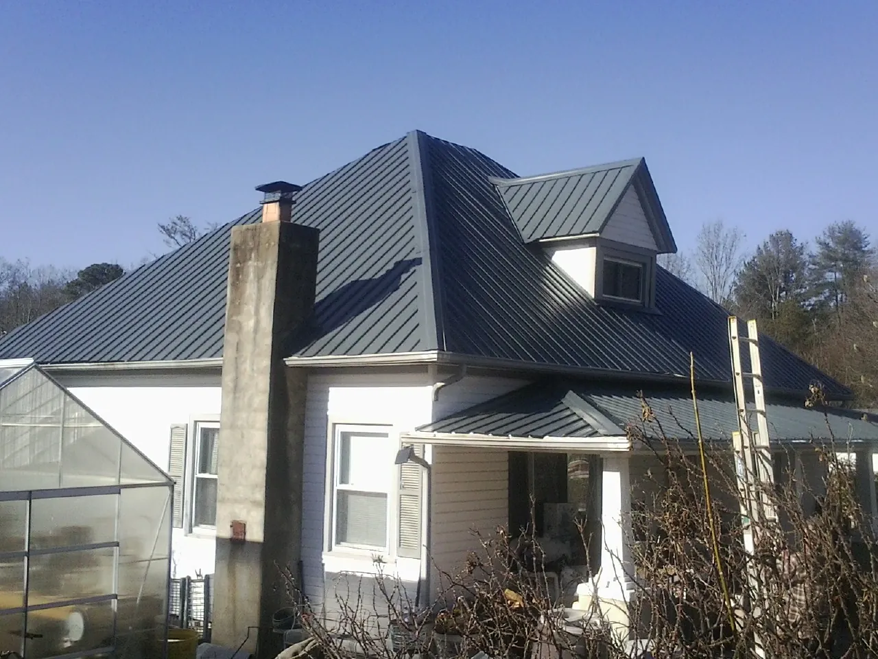Dark blue standing seam metal roof on a white farmhouse with dormer — Slate & Tile Roof Repair by Roofing Brothers in Shiro