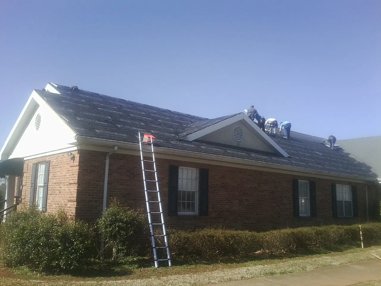 Crew tearing shingles off a brick ranch roof with a ladder set — Emergency Roof Repair work by our crew in Shiro