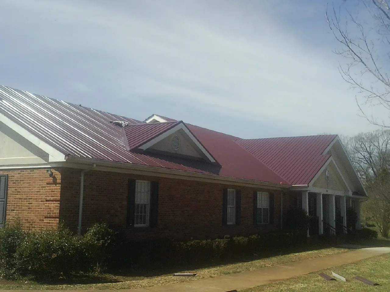 Red metal roof with gabled entries on a long brick building, from a Hail Damage Roof Repair job in Shiro
