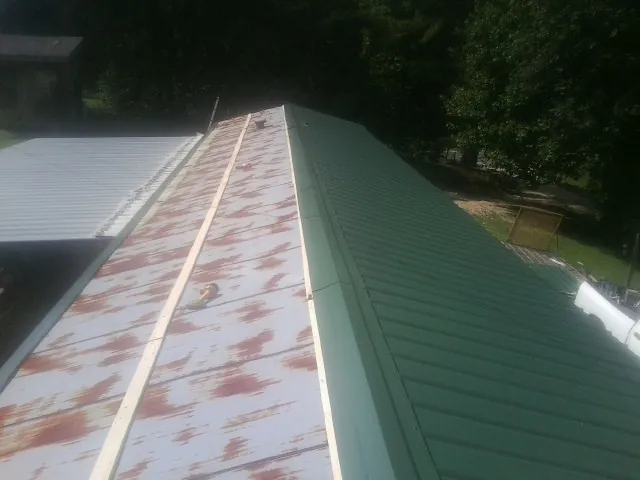 Old rusted panels beside newly installed green metal roofing — Wind Damage Roof Repair by Roofing Brothers in Shiro