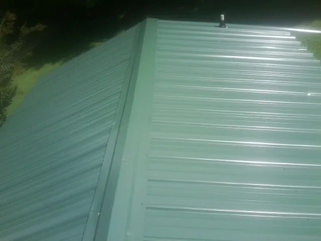 New green metal panels meeting at the ridge of a roof — Flat Roof Repair work by our crew in Shiro
