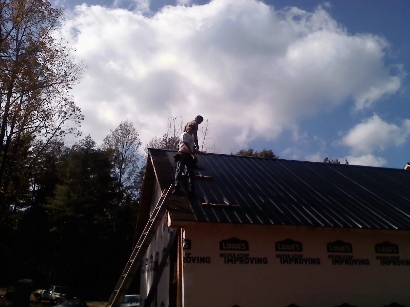 Roofer fastening dark metal panels high against a cloudy sky, from a Roof Inspection job in Shiro