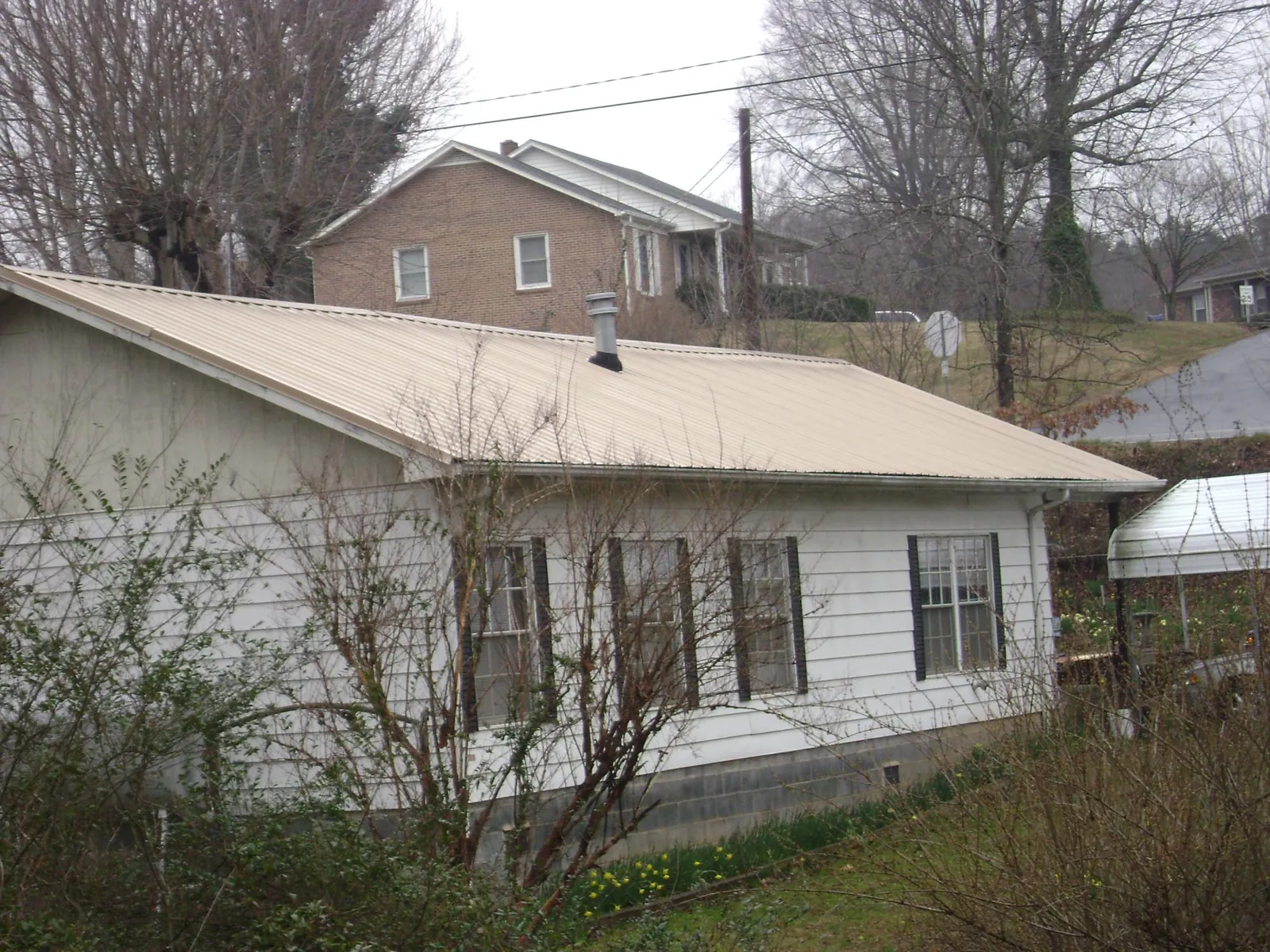 Tan metal roof on a white sided house set into a hillside — Commercial Roofing by Roofing Brothers in Shiro