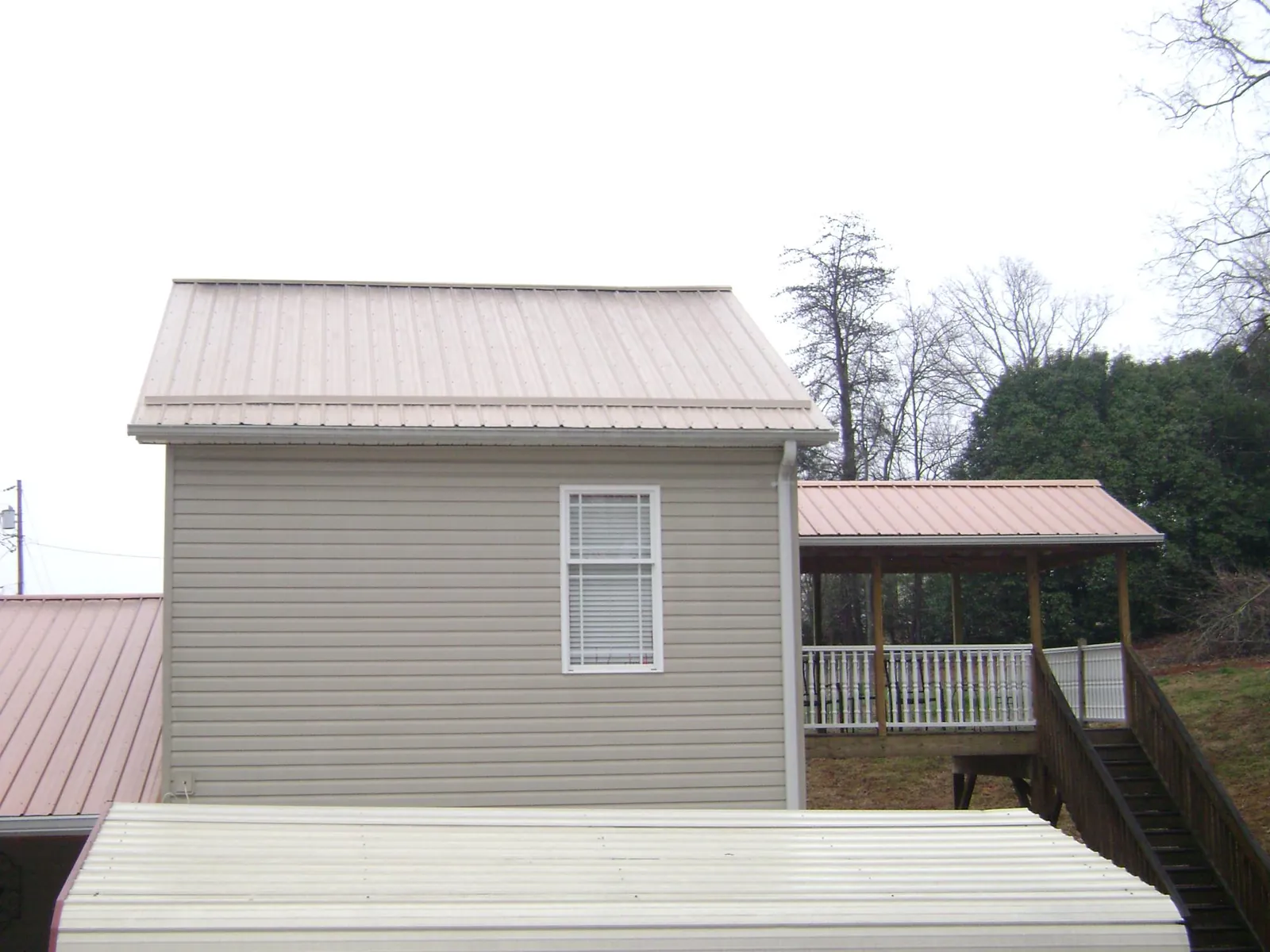 Tan metal roofs on a two story addition and attached porch, from a Roof Replacement job in Shiro