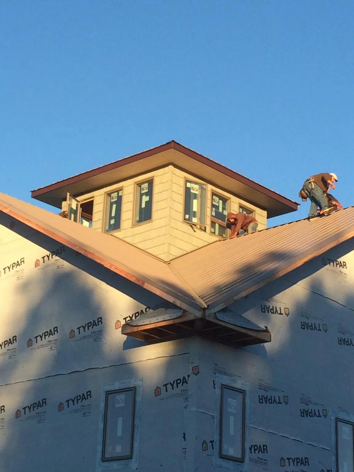Roofers working around a rooftop cupola on a new metal roof at sunset — Roof Waterproofing in Shiro by Roofing Brothers